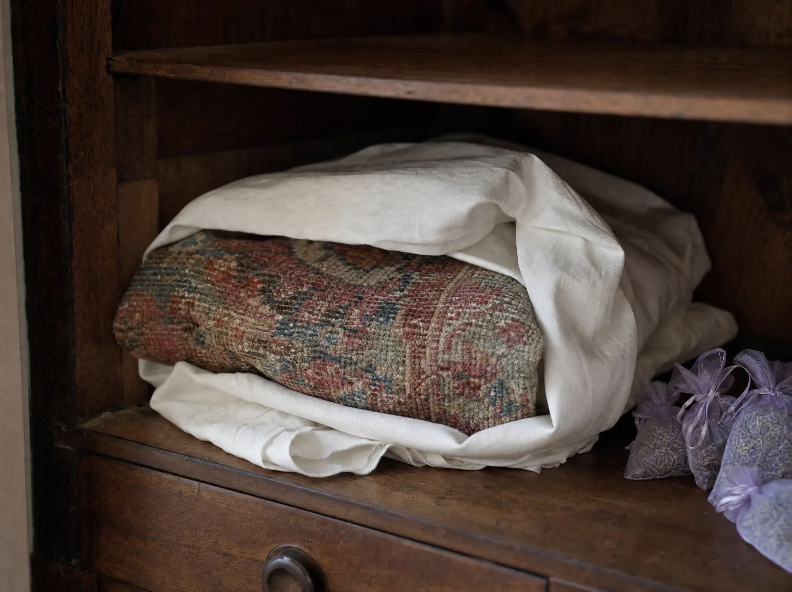 Tapis plié dans un drap de coton rangé sur l'étagère d'une armoire, sachets de lavande (illustration)