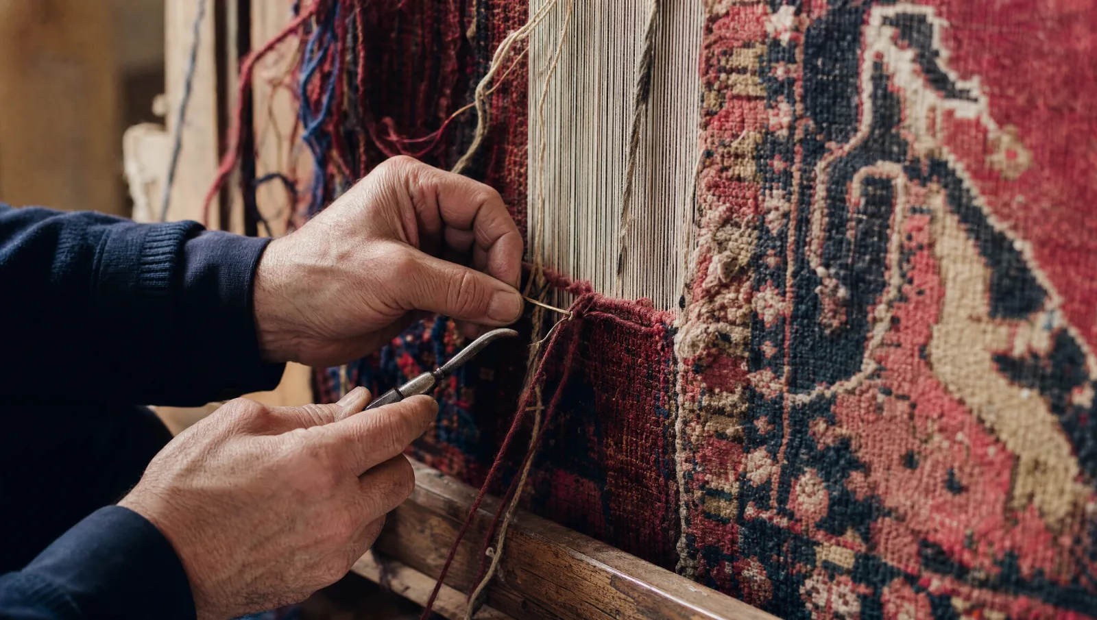 Reprise de trame à la main : nœuds de laine bordeaux, bleu marine et beige noués sur un tapis ancien tendu sur un cadre (illustration)