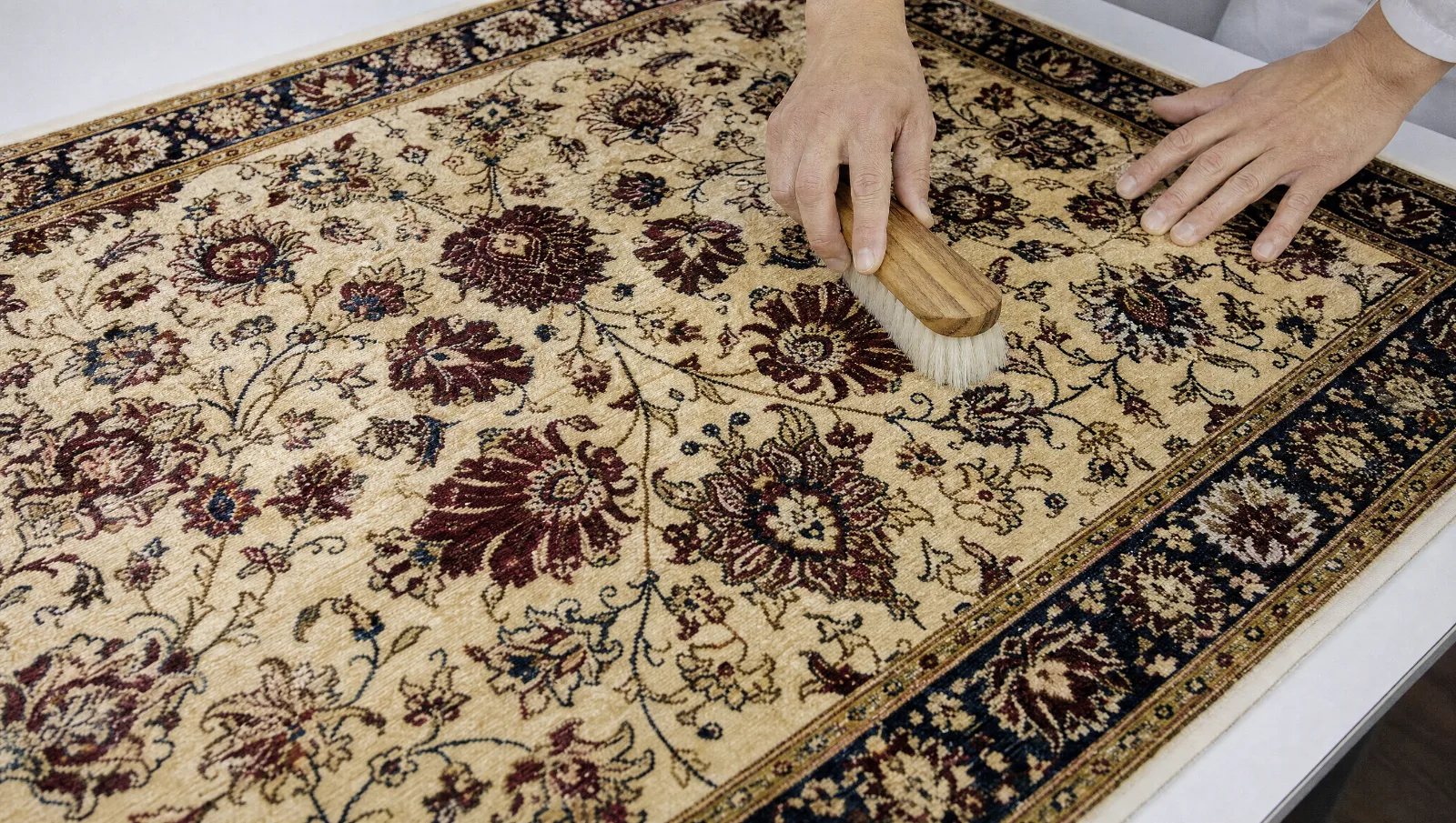 Tapis ancien en soie à motifs floraux brossé délicatement à la brosse très douce sur une table claire (illustration)
